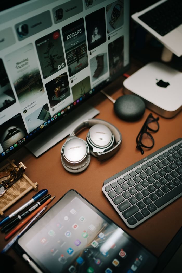 A neatly organized home office setup featuring tablets, headphones, and eyeglasses for a productive environment.