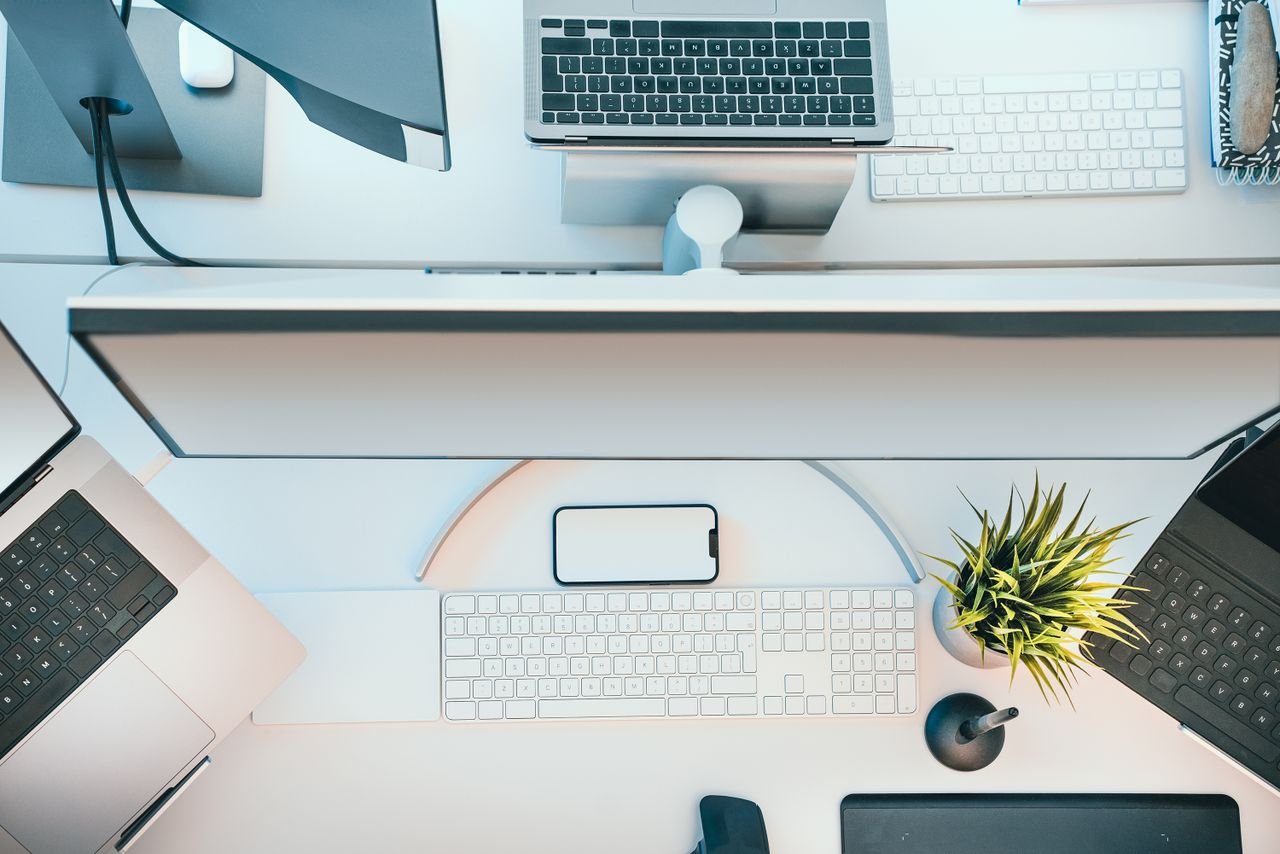 Top view of a modern tech workspace featuring laptops, keyboards, and a potted plant.